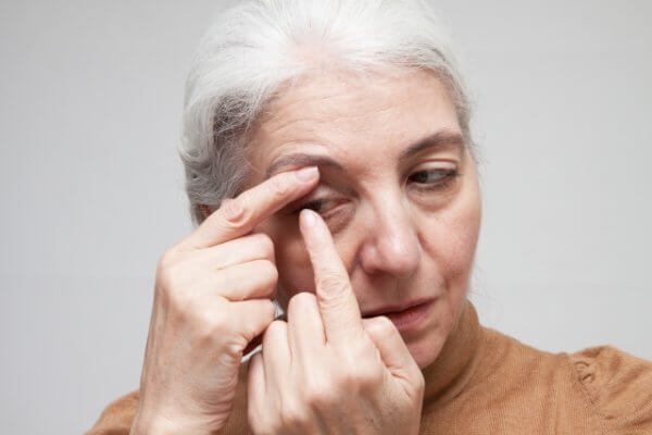 An older woman inserting a contact lens into her right eye.