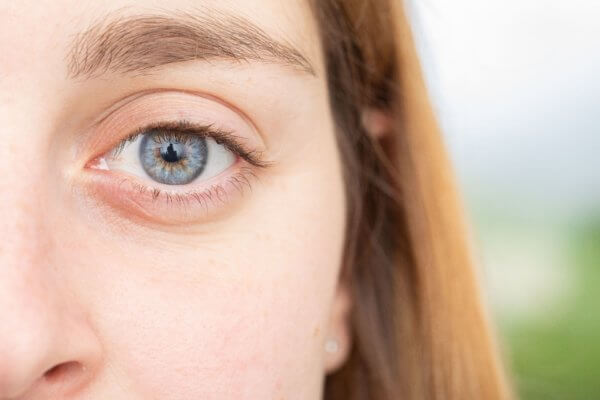  Close-up of a woman's blue eye with light skin and light brown hair visible in the background.